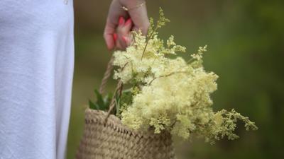 Woman holding flowers in basketweave bag